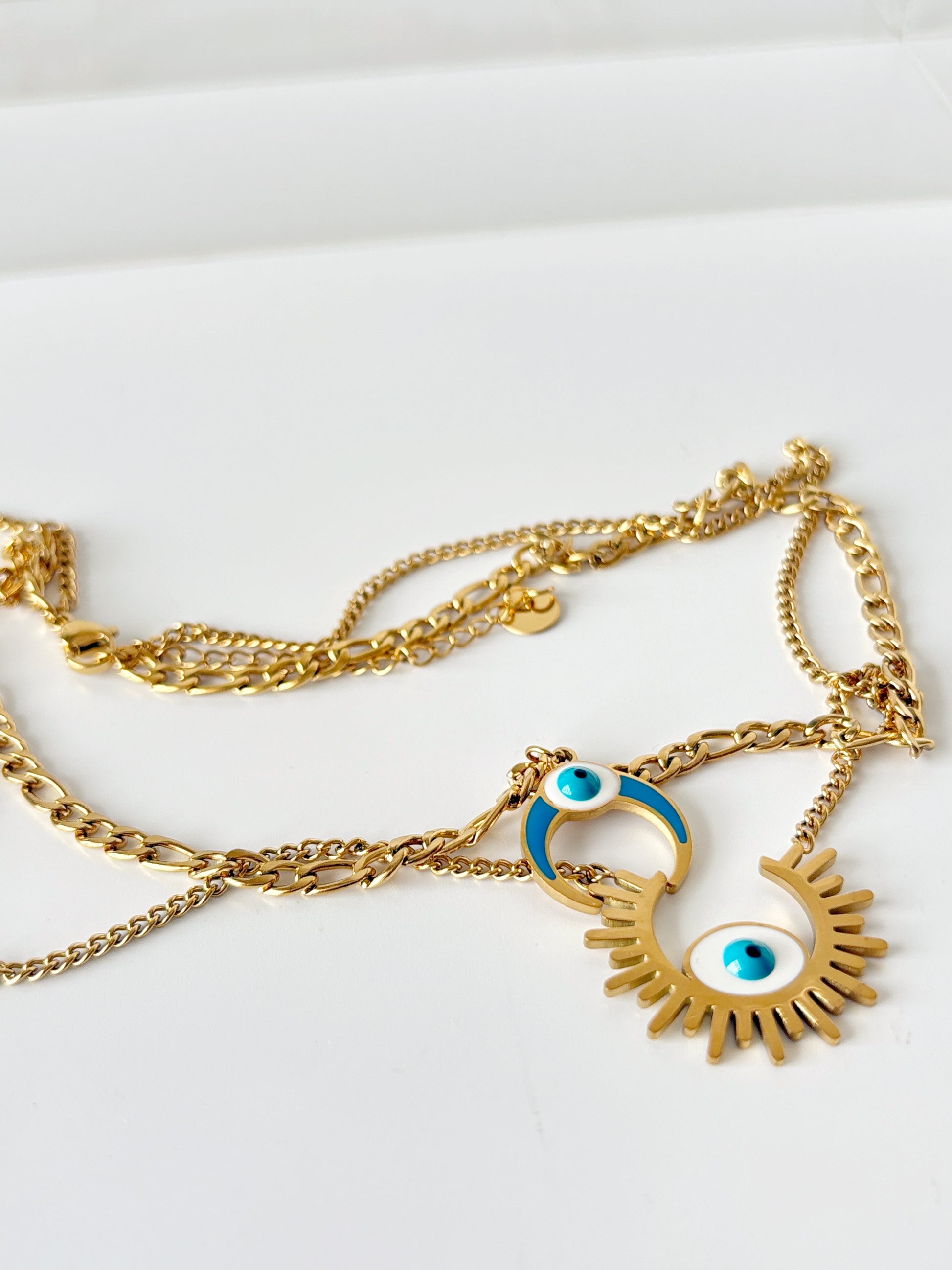 Gold necklace with evil eye and moon design on a white background