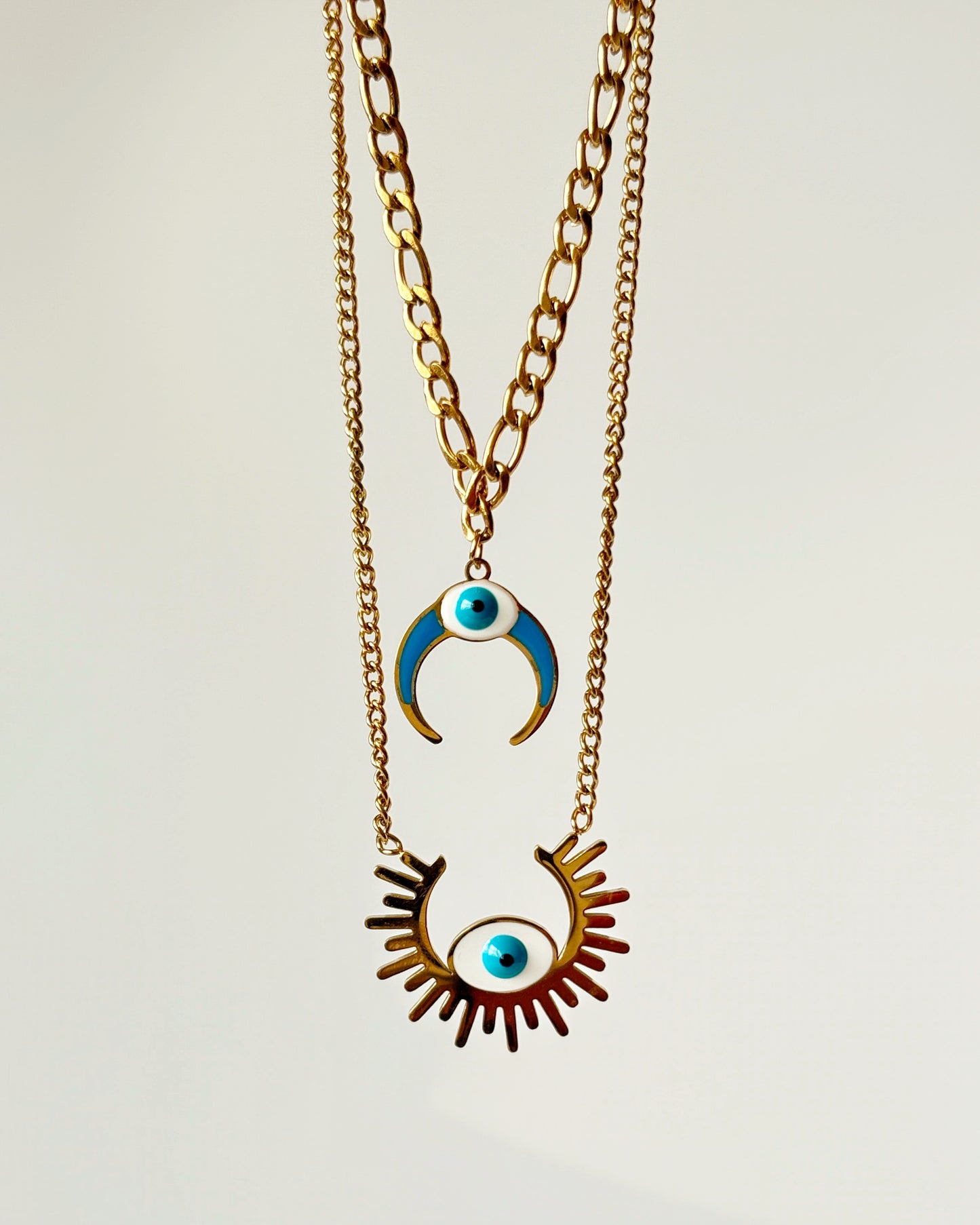Two-layered Necklace with eye-shaped pendant and crescent moon pendant on a light gray background