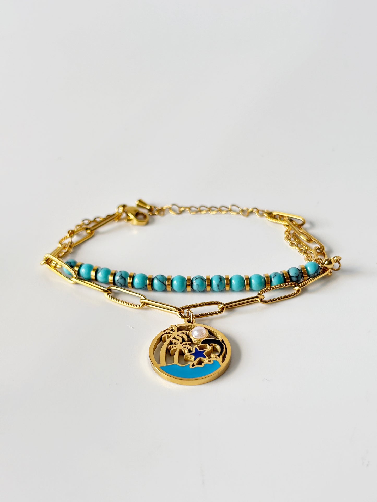 Gold bracelet with turquoise beads and a charm on a light grey background