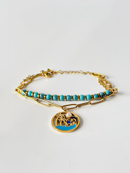 Gold bracelet with turquoise beads and a charm on a light grey background