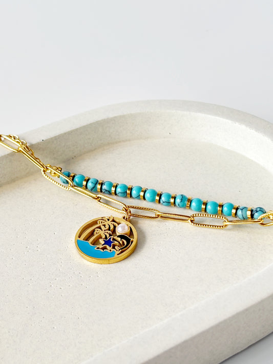 Bracelet with turquoise beads and gold charm on a white surface